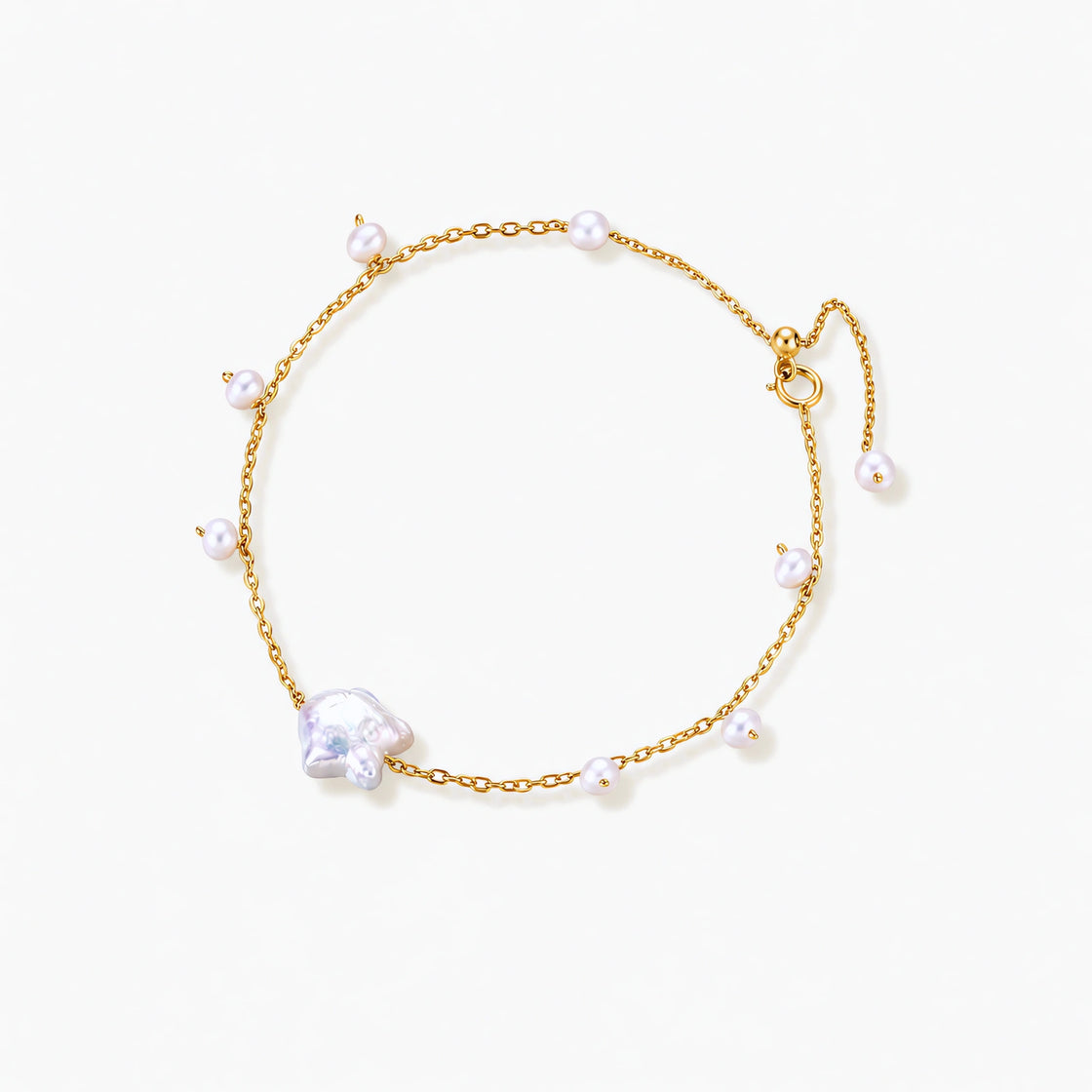 Delicate gold chain bracelet with baroque pearl centerpiece and small freshwater pearls on cream background.