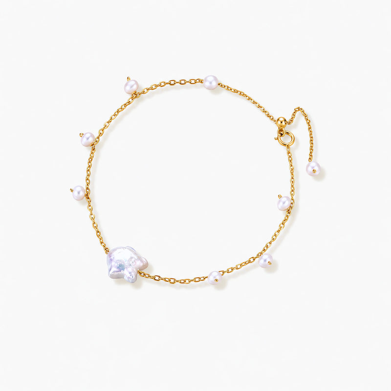 Delicate gold chain bracelet with baroque pearl centerpiece and small freshwater pearls on cream background.