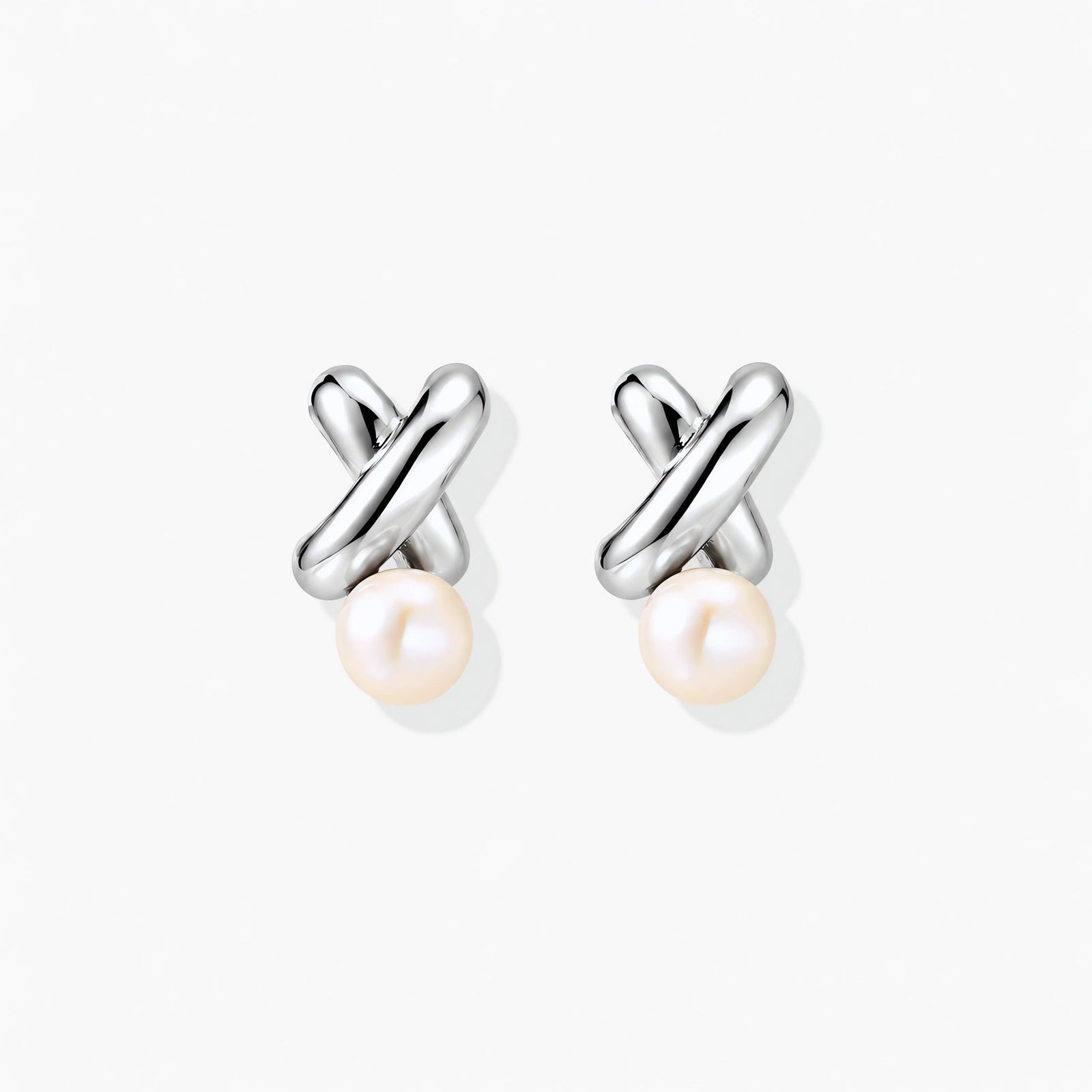 Rhodium-plated silver earrings with twisted X design and freshwater pearl drops on beige background
