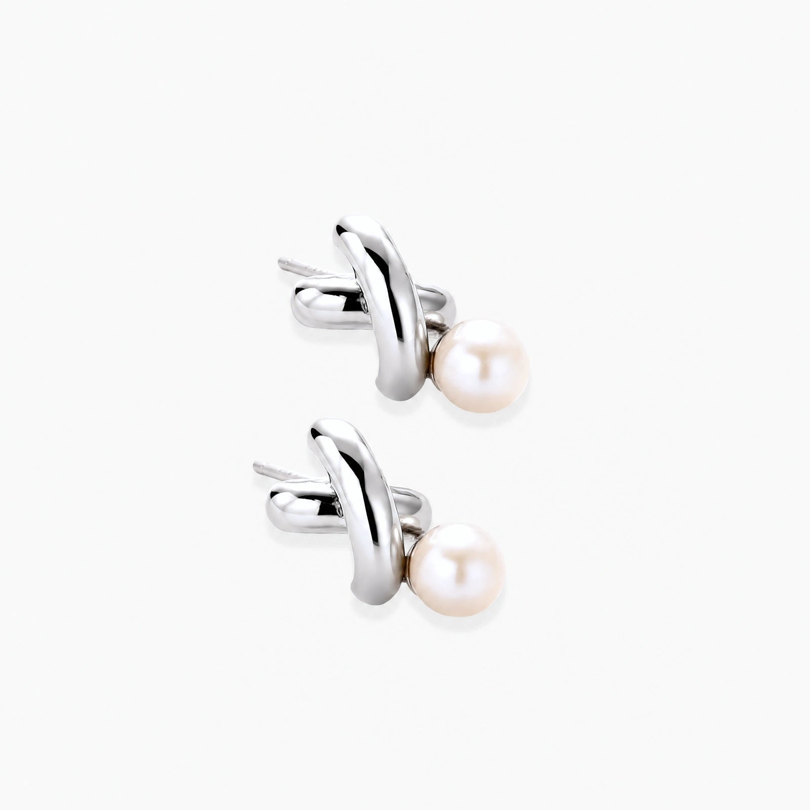 Rhodium-plated silver earrings with twisted X design and freshwater pearl drops on beige background