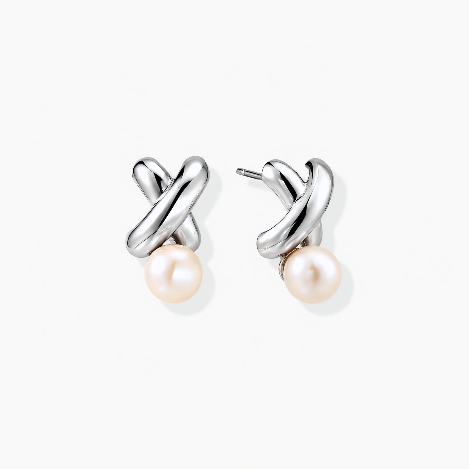 Rhodium-plated silver earrings with twisted X design and freshwater pearl drops on beige background