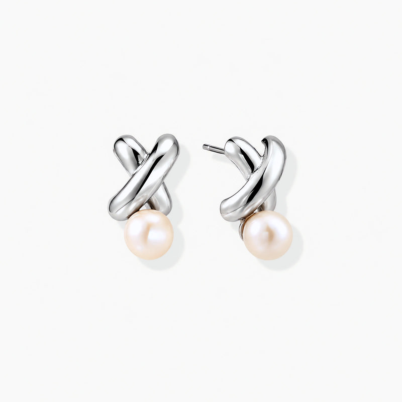 Rhodium-plated silver earrings with twisted X design and freshwater pearl drops on beige background