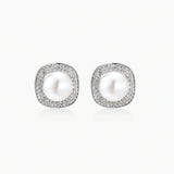 Rhodium-plated sterling silver stud earrings with round freshwater pearls surrounded by geometric crystal halos on cream background.