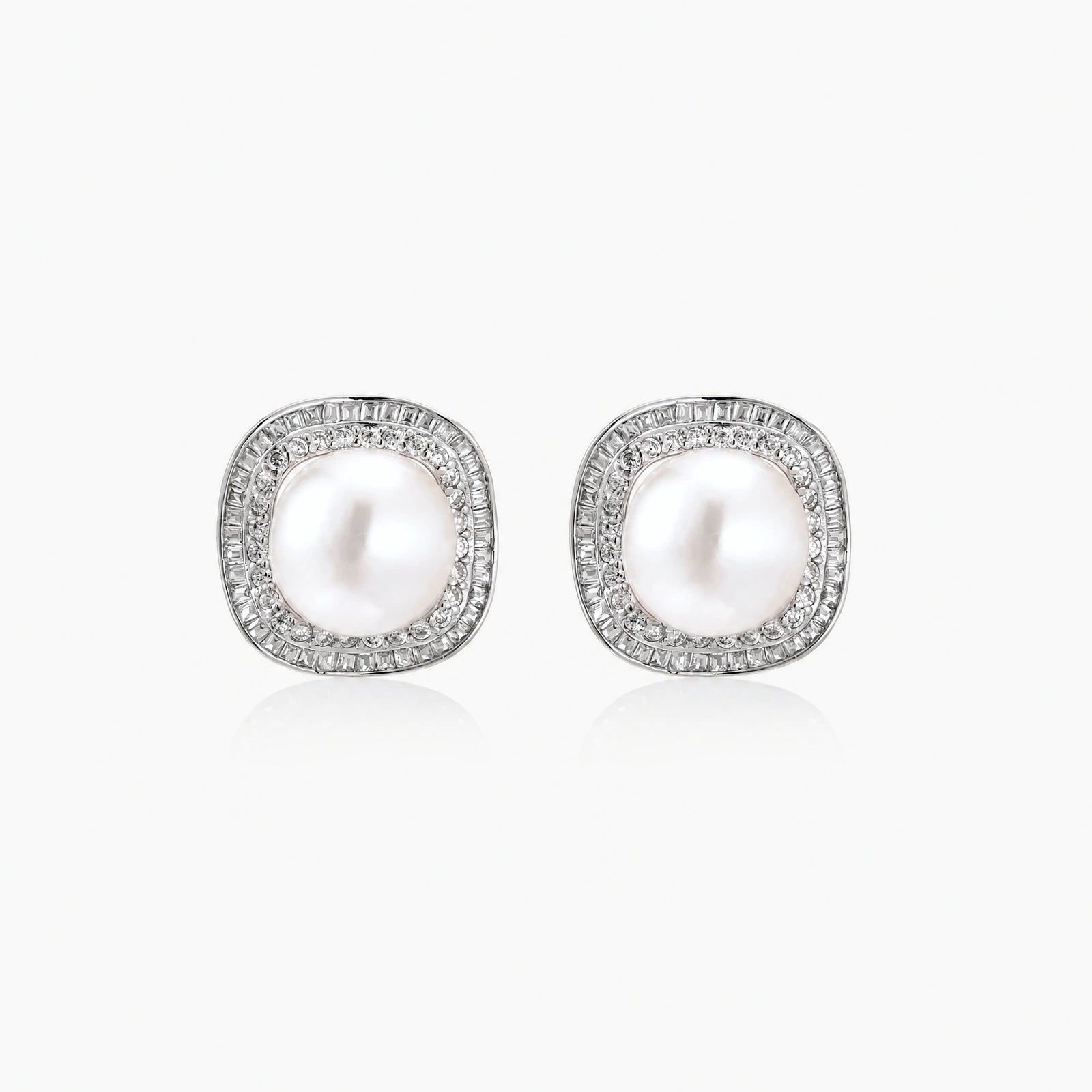 Rhodium-plated sterling silver stud earrings with round freshwater pearls surrounded by geometric crystal halos on cream background.
