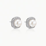 Rhodium-plated sterling silver stud earrings with round freshwater pearls surrounded by geometric crystal halos on cream background.