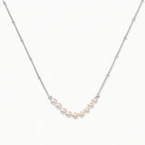 Delicate sterling silver chain necklace with small freshwater pearls arranged in a curved smile arc on cream background.