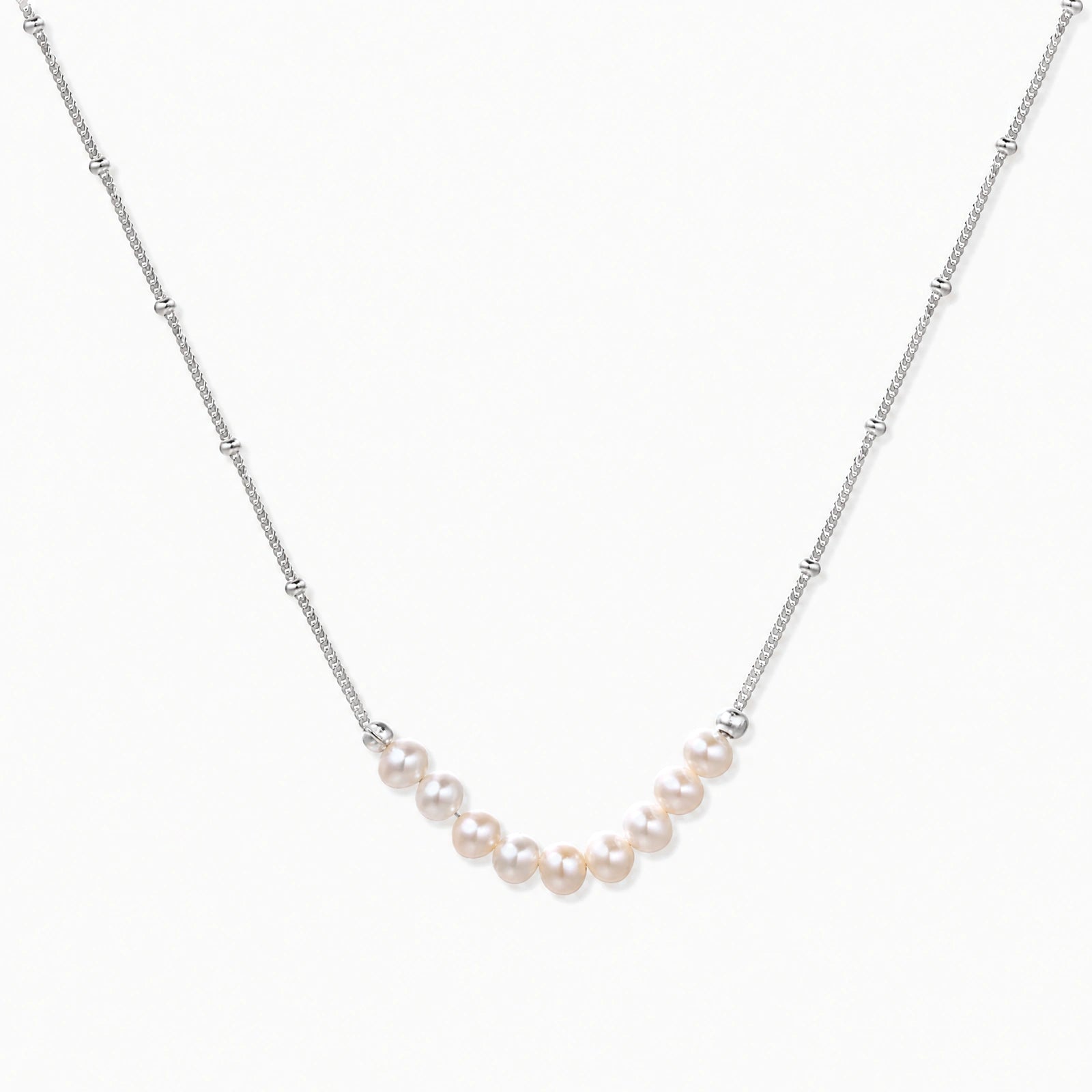 Delicate sterling silver chain necklace with small freshwater pearls arranged in a curved smile arc on cream background.