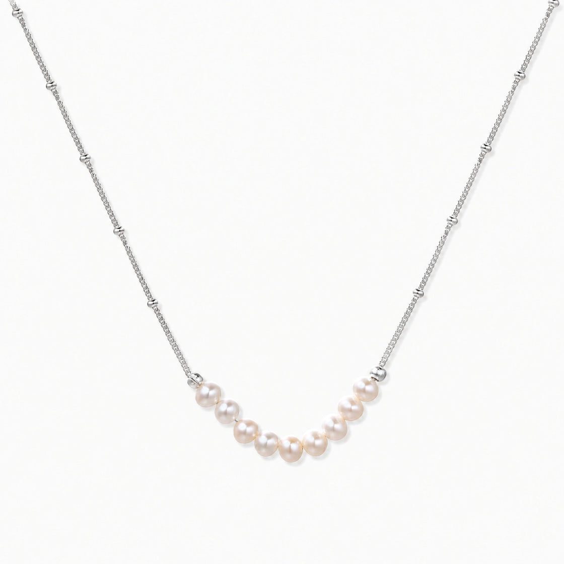 Delicate sterling silver chain necklace with small freshwater pearls arranged in a curved smile arc on cream background.