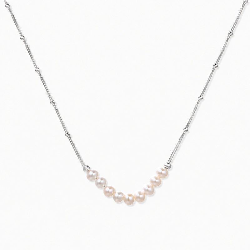 Delicate sterling silver chain necklace with small freshwater pearls arranged in a curved smile arc on cream background.