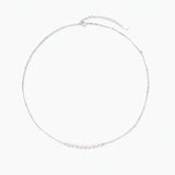 Delicate sterling silver chain necklace with small freshwater pearls arranged in a curved smile arc on cream background.