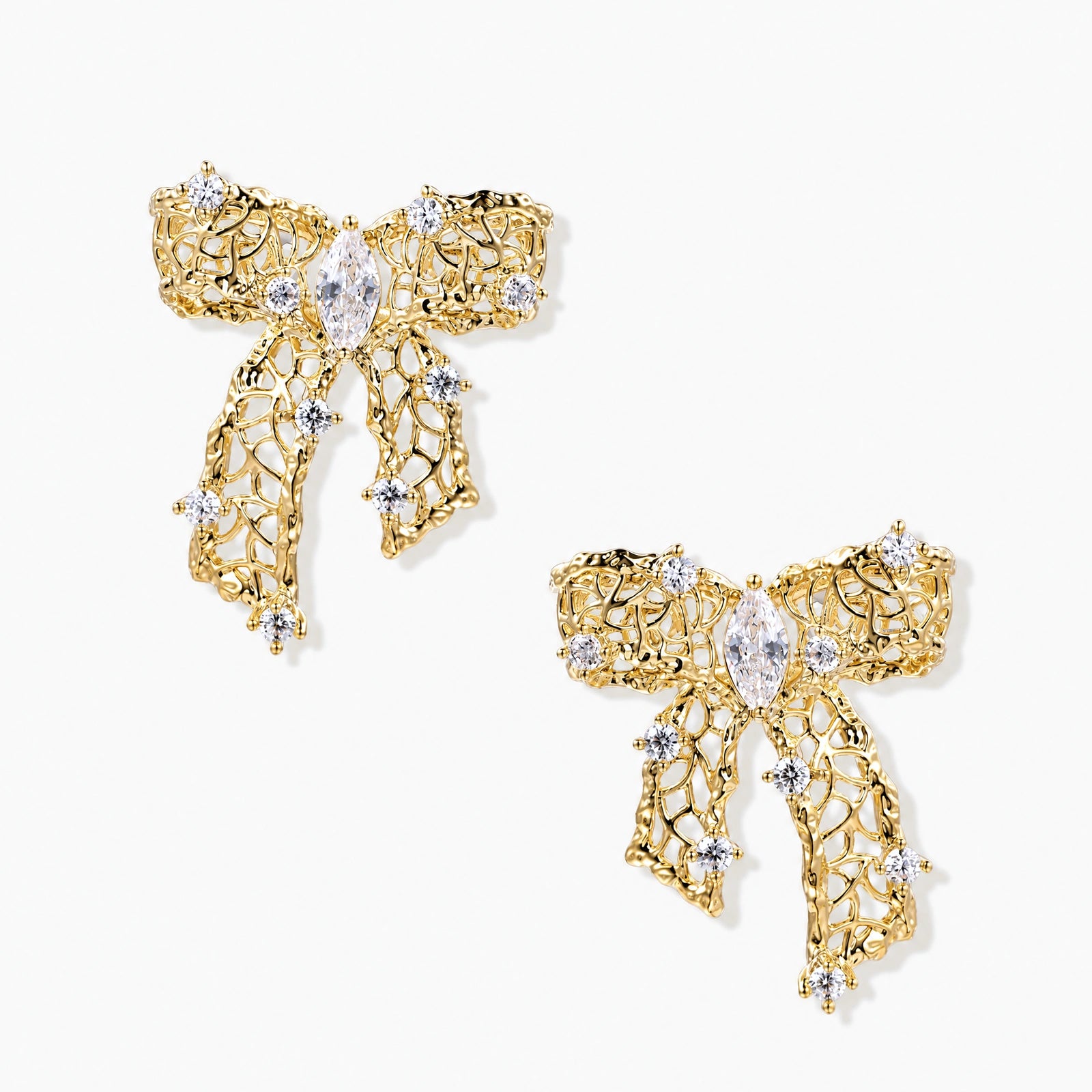 Gold-plated bow earrings with openwork design, marquise center stones, and flowing ribbon tails adorned with zirconia crystals.