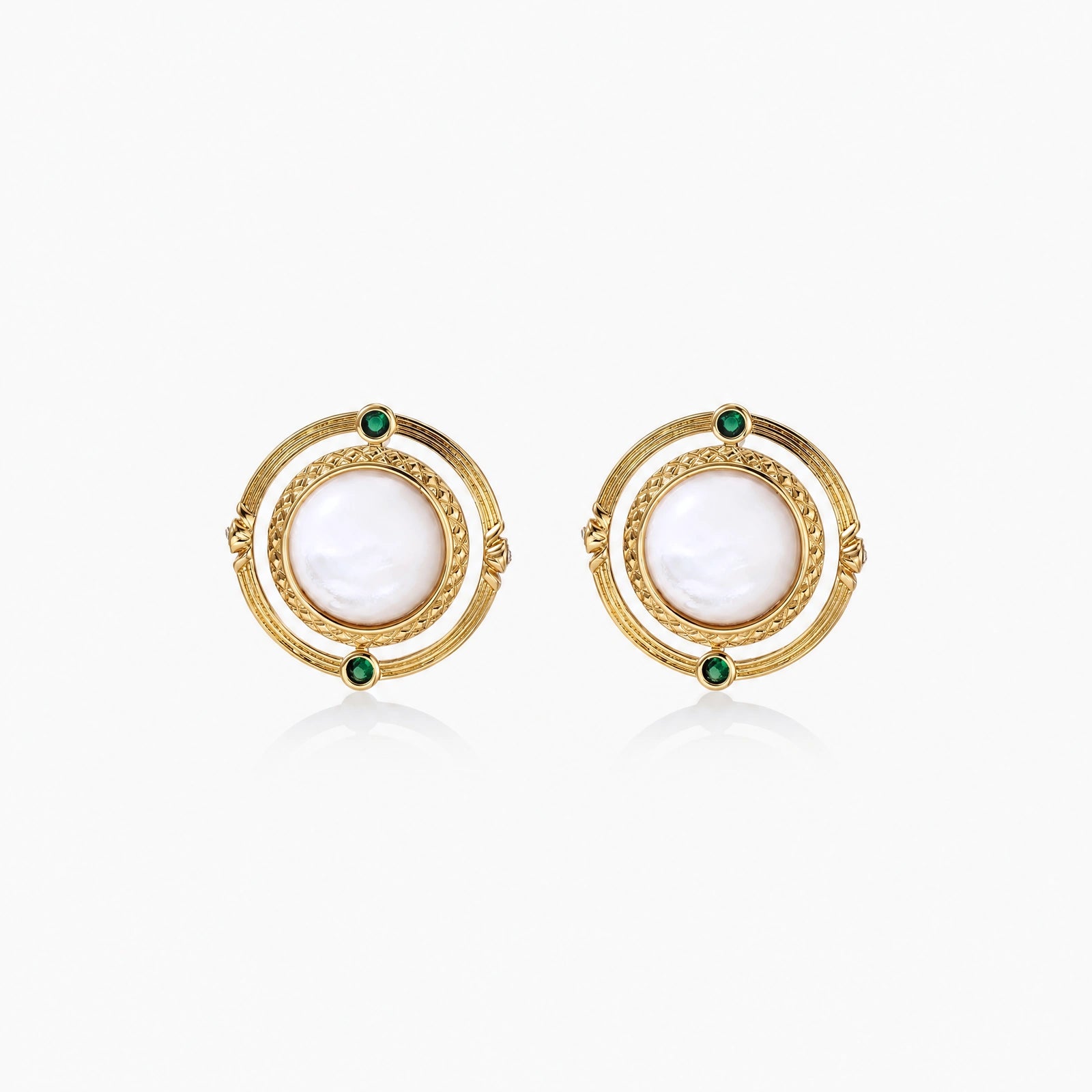 Circular gold stud earrings with iridescent mother-of-pearl center and green zirconia accents on cream background.
