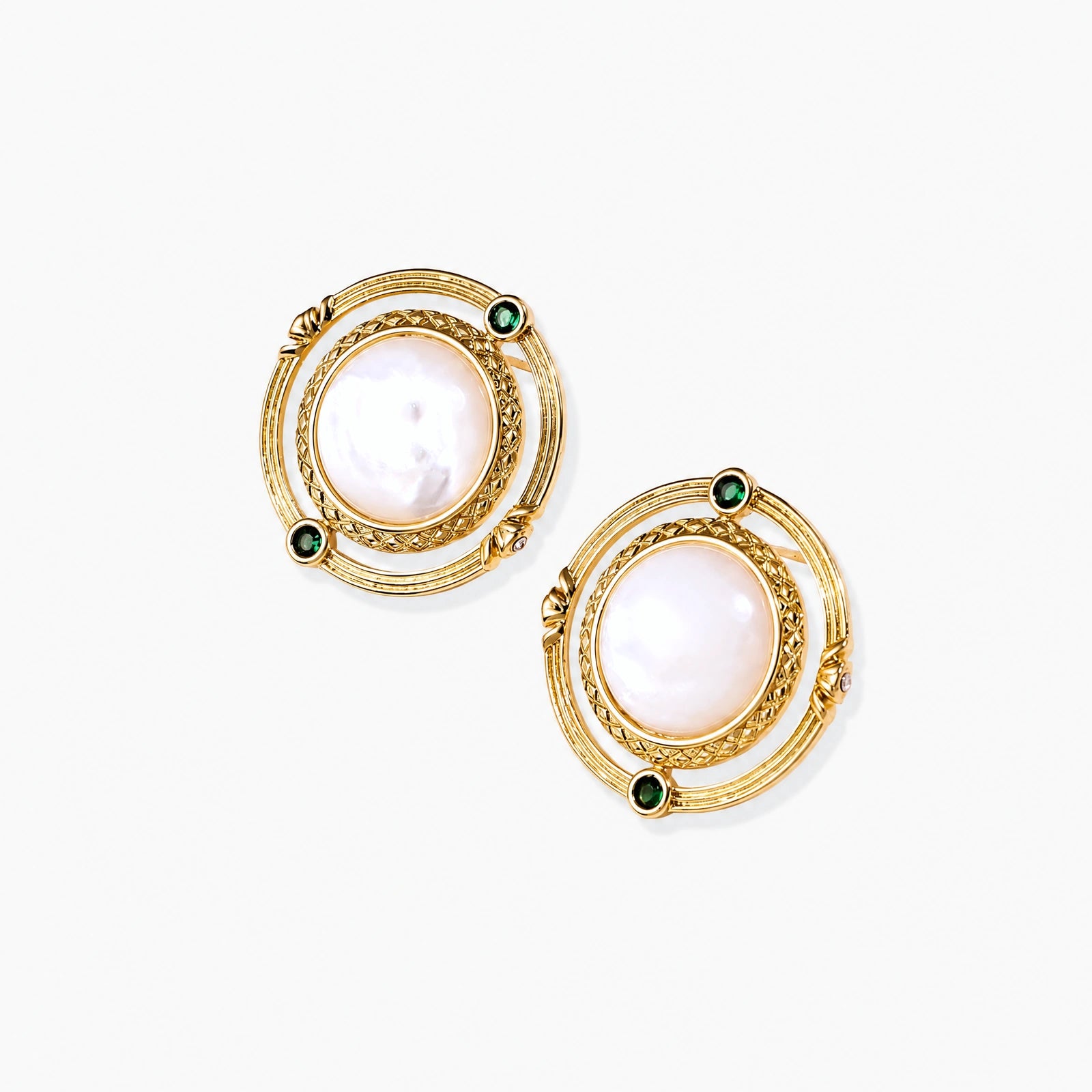 Circular gold stud earrings with iridescent mother-of-pearl center and green zirconia accents on cream background.