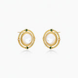 Circular gold stud earrings with iridescent mother-of-pearl center and green zirconia accents on cream background.
