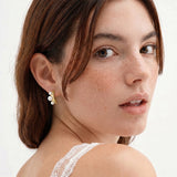 14K gold-plated curved stud earrings with three white freshwater pearls aligned vertically on cream background