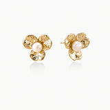 Gold-plated flower stud earrings with textured petals and centered freshwater pearl on beige background
