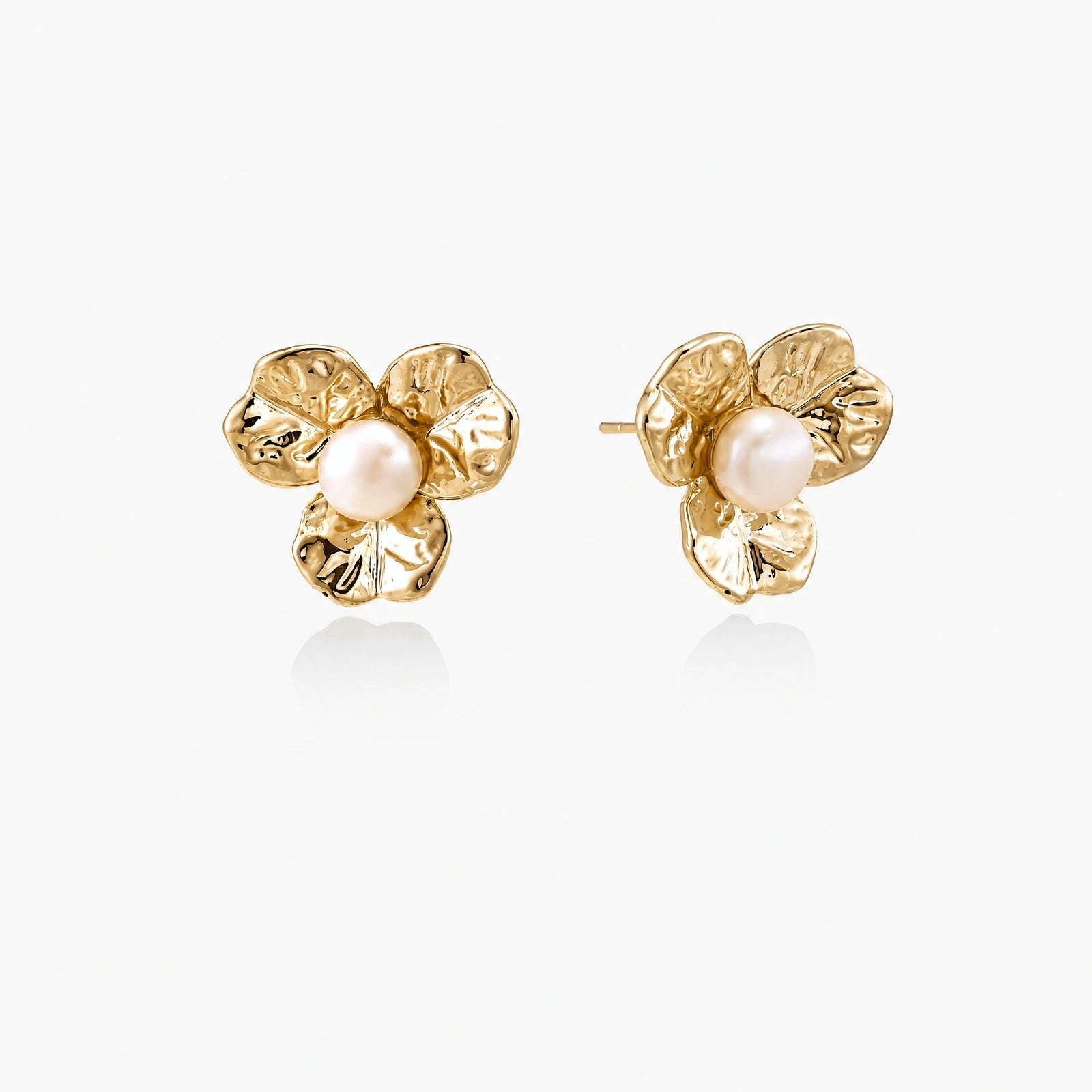 Gold-plated flower stud earrings with textured petals and centered freshwater pearl on beige background
