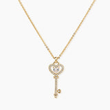 Delicate gold key pendant with heart-shaped bow and crystal pavé detailing on fine chain against cream background.