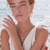 Delicate gold key pendant with heart-shaped bow and crystal pavé detailing on fine chain against cream background.
