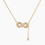 Gold infinity pendant with baguette crystals on adjustable chain against cream background.