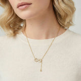 Gold infinity pendant with baguette crystals on adjustable chain against cream background.
