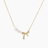 Delicate gold necklace with three white pearls and crystal-embellished bow pendant on cream background