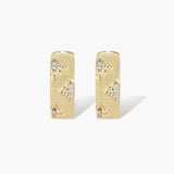 Gold-plated hoop earrings with textured surface and raised floral motifs set with clear zirconia stones on cream background.