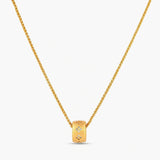 Gold-plated cylindrical ring pendant with brushed finish and scattered crystal accents on a wheat-link chain, cream background.
