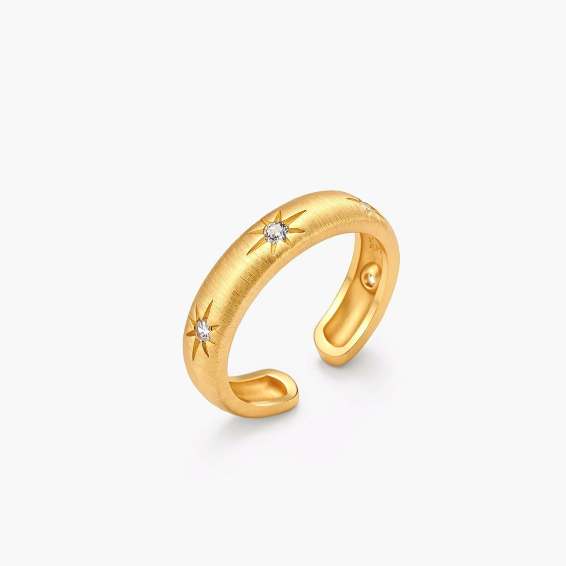 Gold open-band cuff ring with brushed matte finish, engraved 8-point star motifs, and round CZ stones on white background.