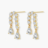 Gold-plated earrings with vertical line of clear crystals and teardrop pendants on neutral background
