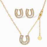 Gold-plated horseshoe necklace and earring set with baguette and round crystals arranged in geometric pattern on white background.