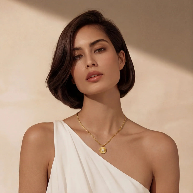 Woman in a white one-shoulder dress wearing a gold sunburst pendant